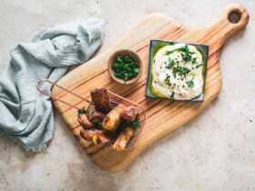 Crispy golden halloumi cheese fries served with a creamy yogurt dipping sauce and fresh herbs on a rustic wooden board