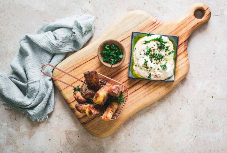 Crispy golden halloumi cheese fries served with a creamy yogurt dipping sauce and fresh herbs on a rustic wooden board