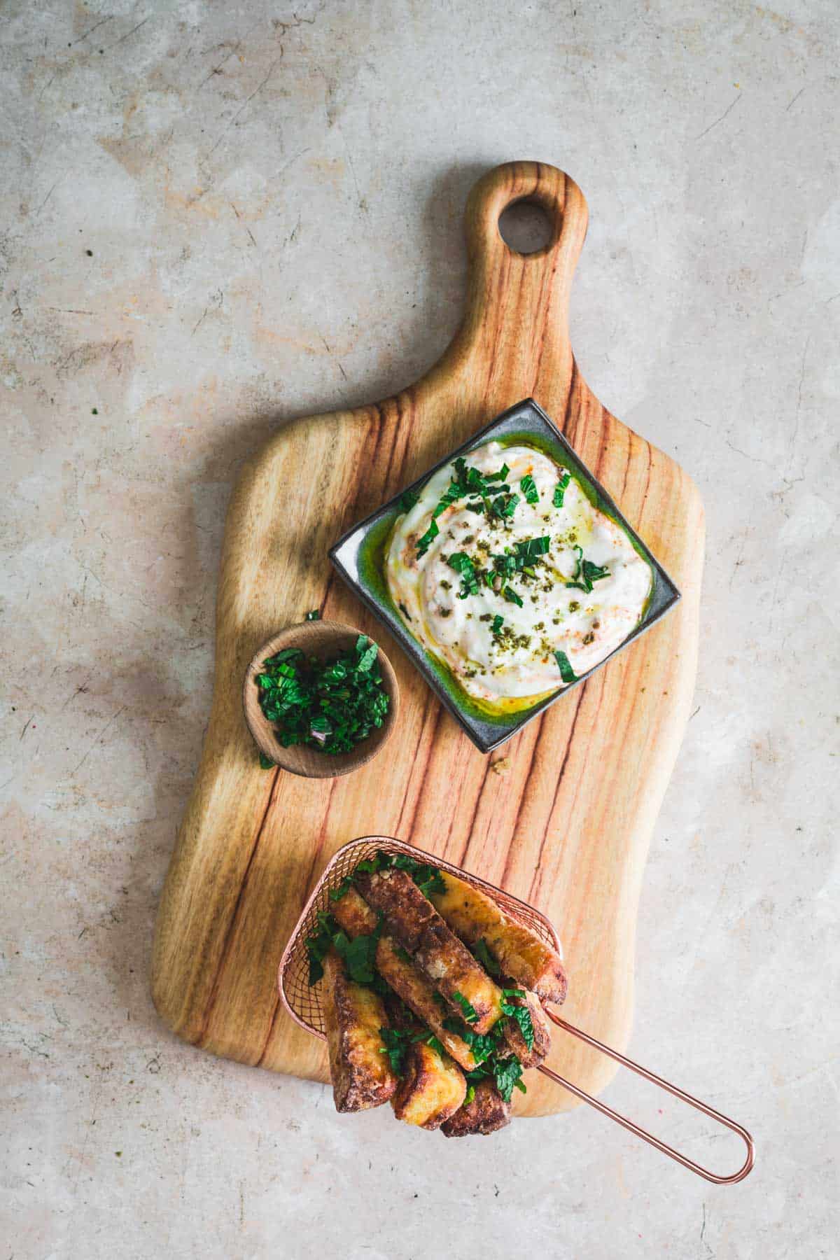 Halloumi cheese block being sliced into thick fry-shaped sticks on a wooden cutting board with spices and olive oil nearby
