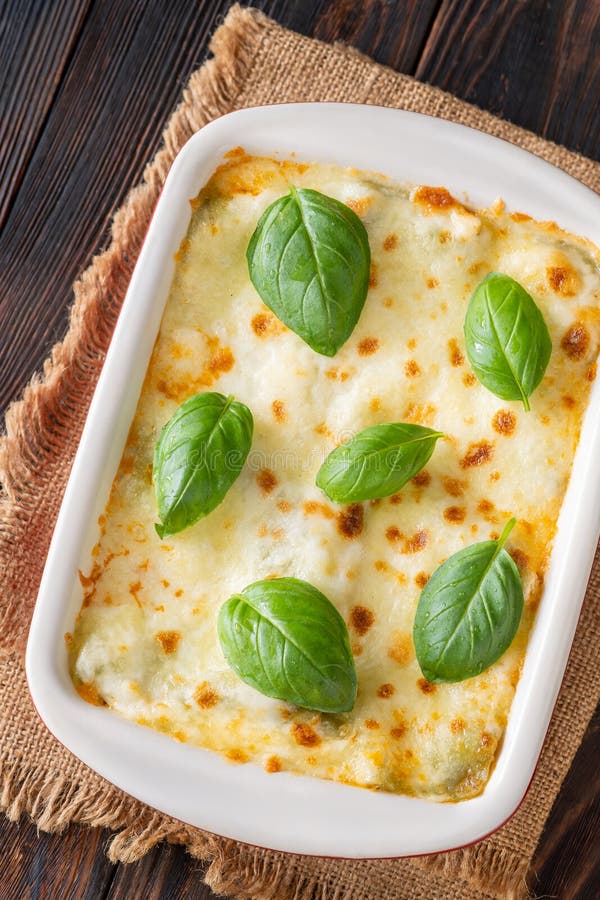 Lasagna Bolognese freshly baked in a white ceramic baking dish with golden bubbling edges and a slice lifted to show rich meaty layers