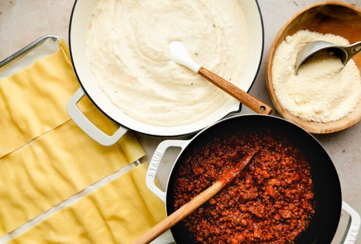 Overhead shot of Lasagna Bolognese ingredients laid out — ground beef and pork, fresh pasta sheets, butter, Parmigiano-Reggiano, vegetables for soffritto, and a saucepan of béchamel
