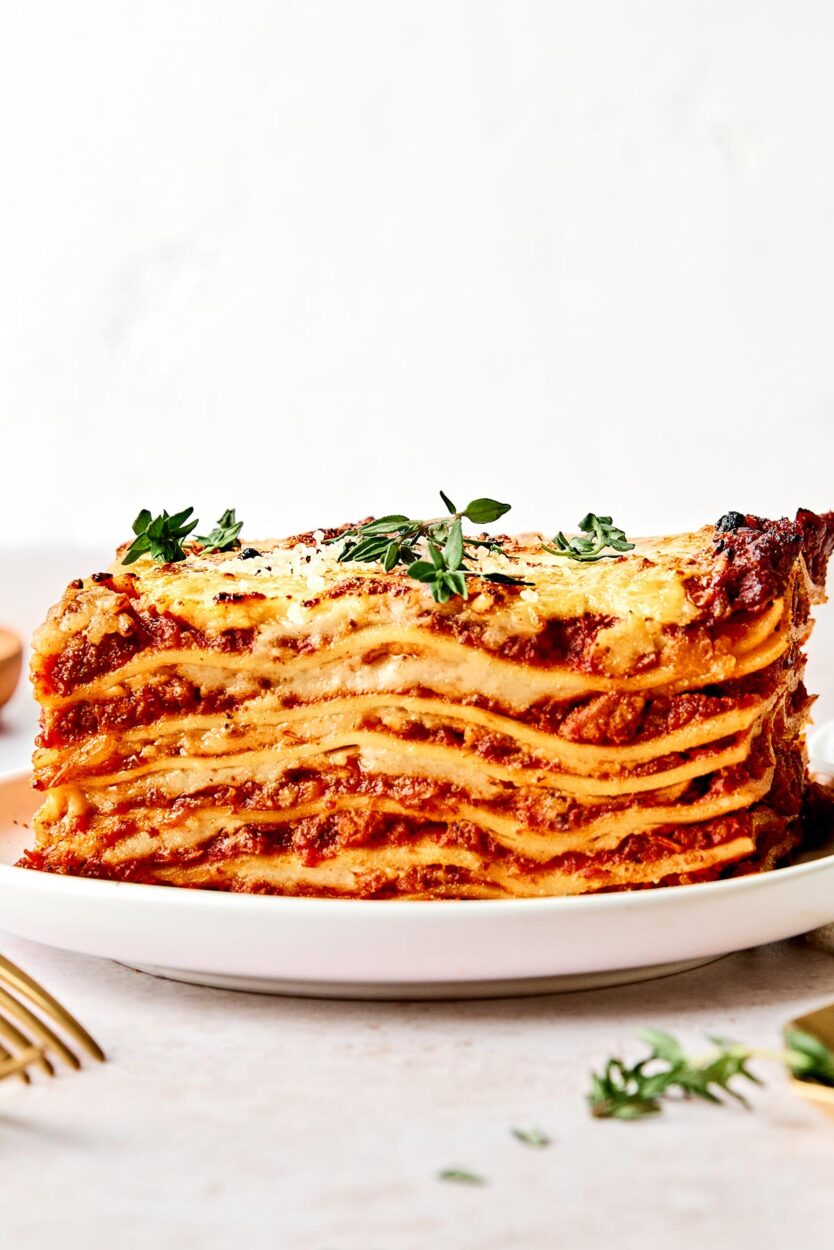 Close-up of a single slice of Lasagna Bolognese on a white plate, showing distinct golden pasta layers, rich meat ragù, and creamy béchamel with a Parmigiano crust on top