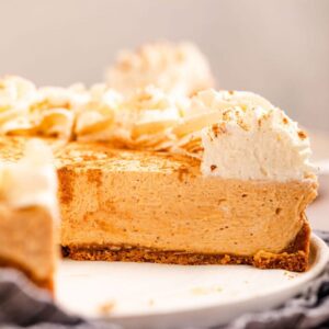 Close-up slice of no bake pumpkin cheesecake on a plate showing the creamy orange filling and graham cracker crust layers