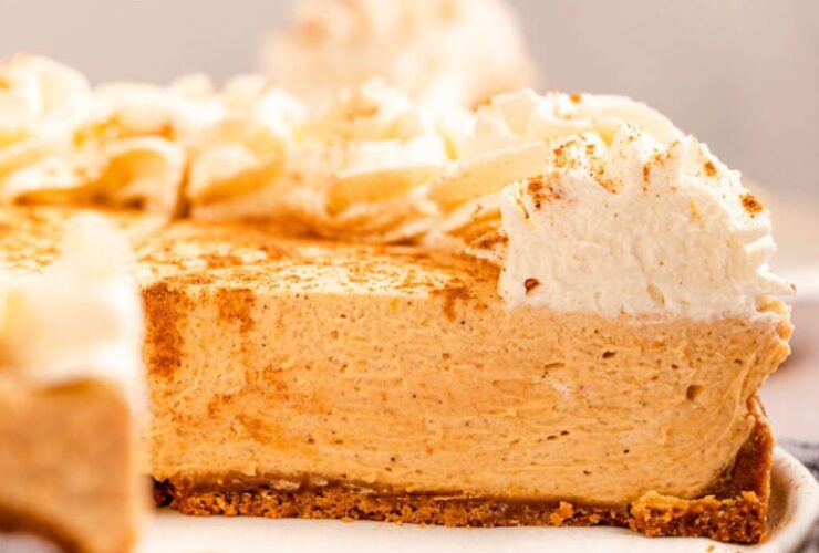 Close-up slice of no bake pumpkin cheesecake on a plate showing the creamy orange filling and graham cracker crust layers