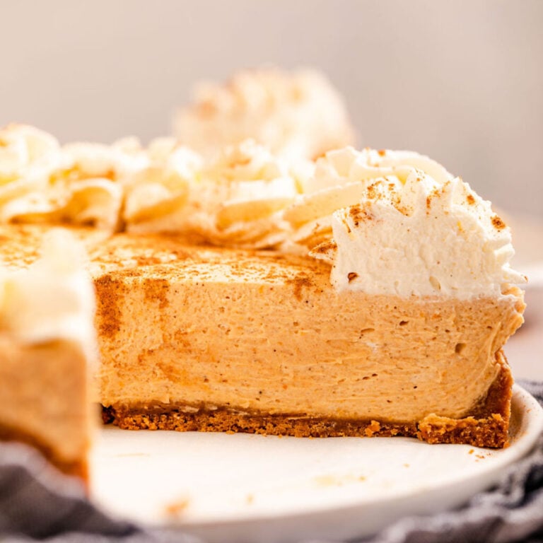 Close-up slice of no bake pumpkin cheesecake on a plate showing the creamy orange filling and graham cracker crust layers