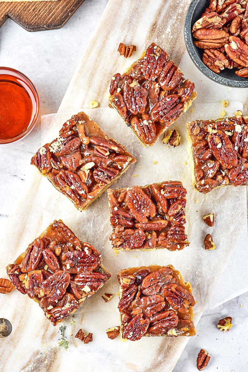 Overhead flat-lay of pecan pie bar ingredients — brown sugar, pecans, eggs, butter, corn syrup, flour — on a marble surface