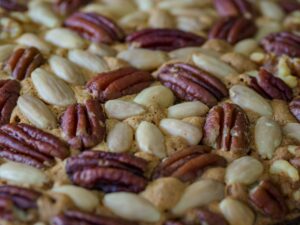 Close-up of a single pecan pie bar showing the layered cross-section — golden shortbread base, dense caramel pecan filling, light flaky sea salt on top