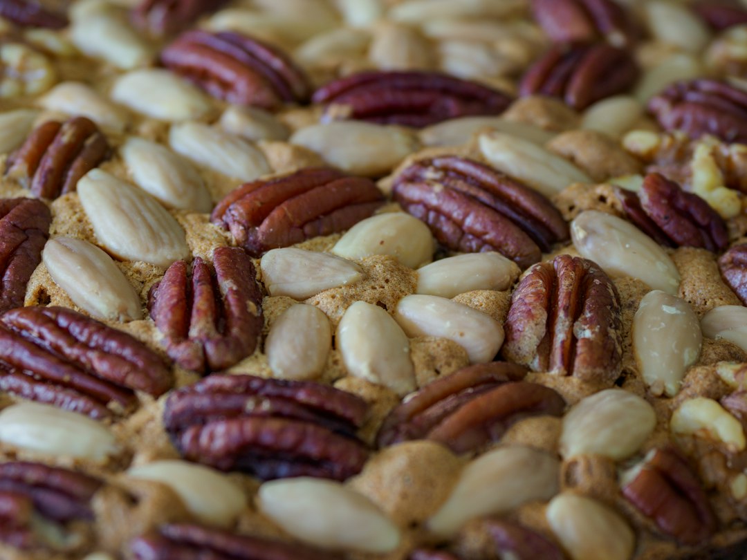 Close-up of a single pecan pie bar showing the layered cross-section — golden shortbread base, dense caramel pecan filling, light flaky sea salt on top
