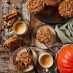 Overhead flat-lay of pumpkin muffin ingredients — pumpkin purée, chocolate chips, brown sugar, eggs, flour, and spices on a wooden surface