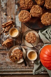 Overhead flat-lay of pumpkin muffin ingredients — pumpkin purée, chocolate chips, brown sugar, eggs, flour, and spices on a wooden surface