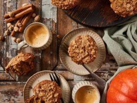 Overhead flat-lay of pumpkin muffin ingredients — pumpkin purée, chocolate chips, brown sugar, eggs, flour, and spices on a wooden surface