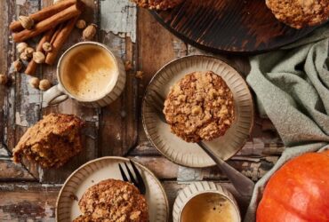 Overhead flat-lay of pumpkin muffin ingredients — pumpkin purée, chocolate chips, brown sugar, eggs, flour, and spices on a wooden surface
