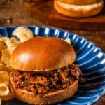 Overhead flat-lay of sloppy joe ingredients including ground beef, tomato paste, ketchup, brown sugar, apple cider vinegar, Worcestershire sauce, diced onion and bell pepper laid out on a dark slate surface