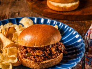 Overhead flat-lay of sloppy joe ingredients including ground beef, tomato paste, ketchup, brown sugar, apple cider vinegar, Worcestershire sauce, diced onion and bell pepper laid out on a dark slate surface