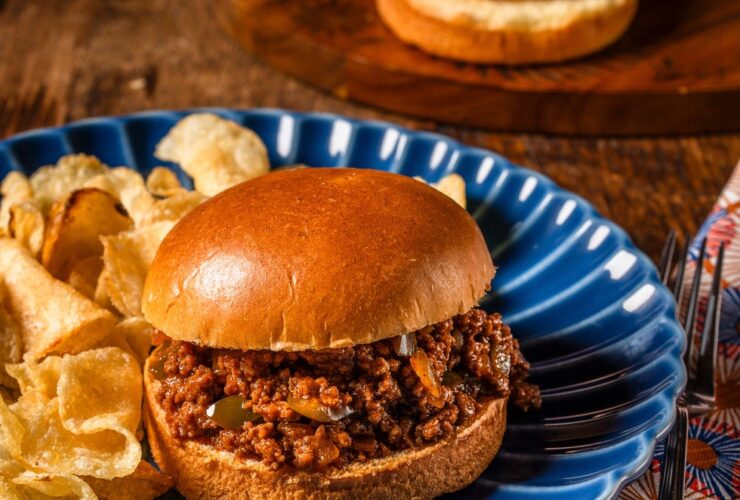 Overhead flat-lay of sloppy joe ingredients including ground beef, tomato paste, ketchup, brown sugar, apple cider vinegar, Worcestershire sauce, diced onion and bell pepper laid out on a dark slate surface
